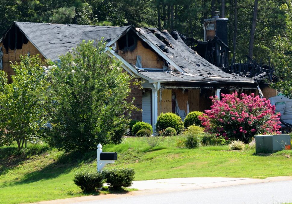 Fire-damaged home exterior after a house fire, showing roof damage and the need for restoration services.